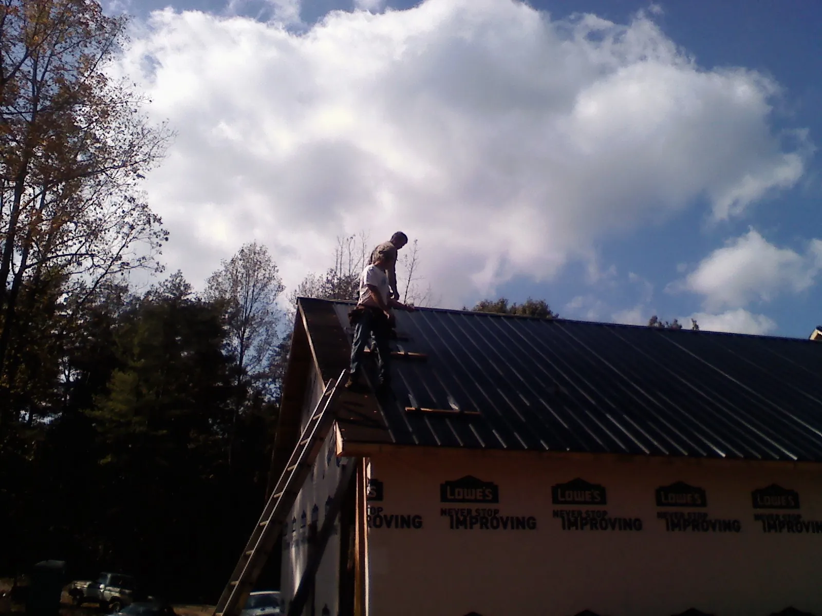 Roofer fastening dark metal panels high against a cloudy sky, from a Roof Inspection job in Paterson