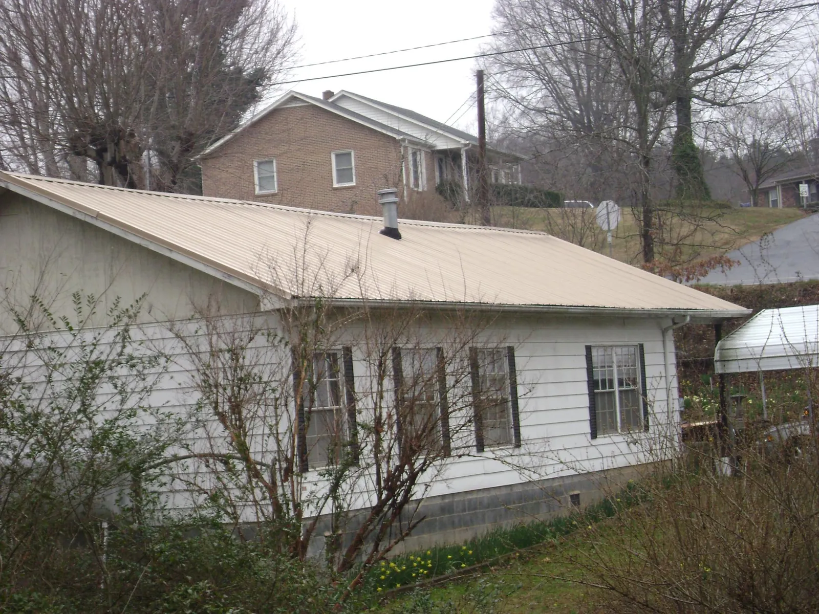 Tan metal roof on a white sided house set into a hillside — Commercial Roofing by Roofing Brothers in Paterson