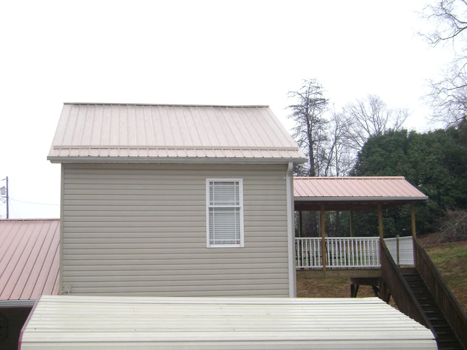 Tan metal roofs on a two story addition and attached porch, from a Roof Replacement job in Paterson